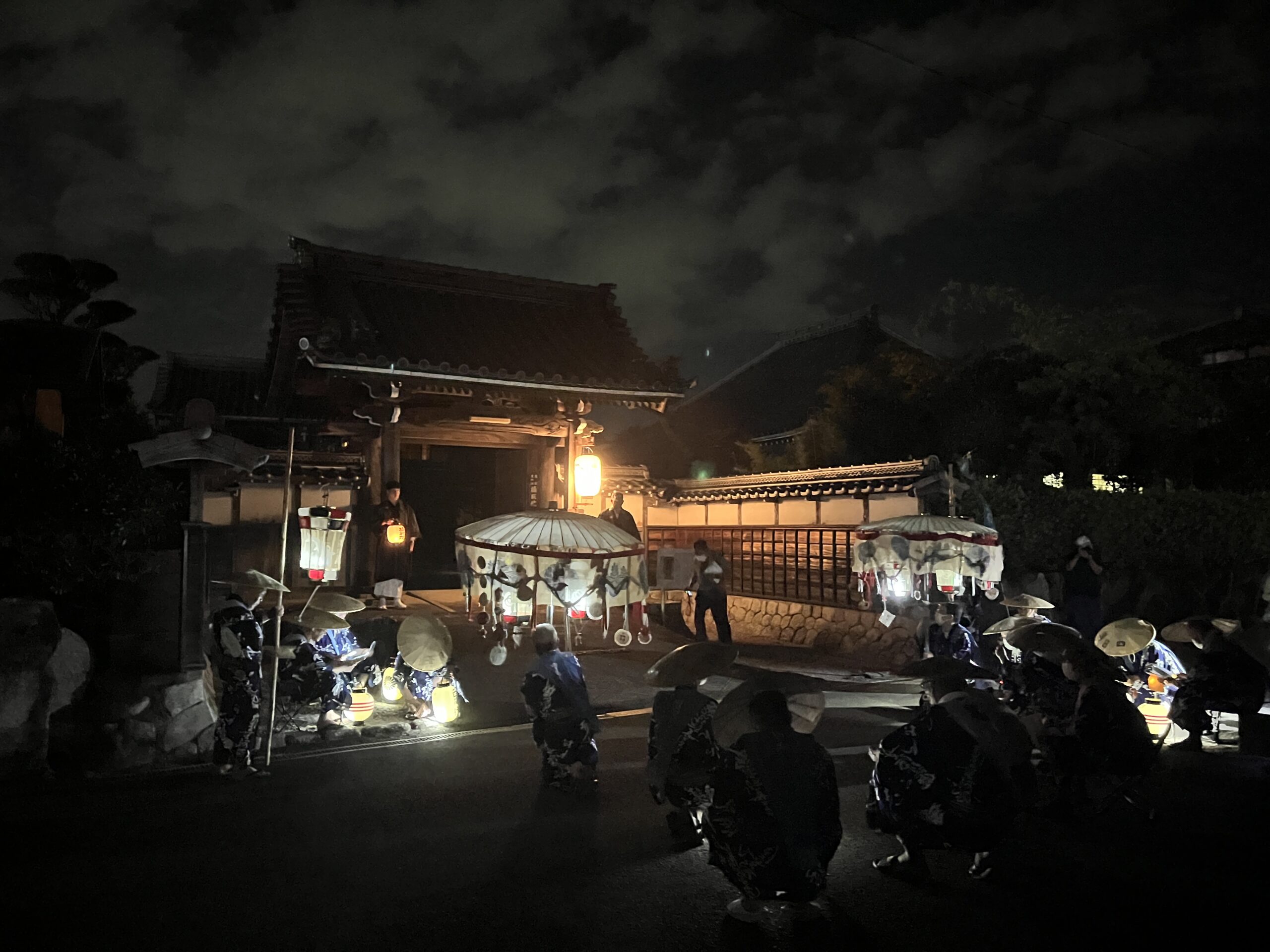 三日市の「おんない会」の様子。夜の寺門前で、提灯の灯りの中、集う人たち。
